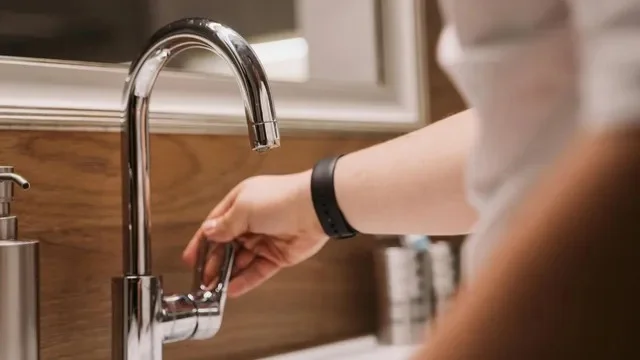 A person’s hand turning a modern chrome bathroom faucet, with no water flowing from the tap.